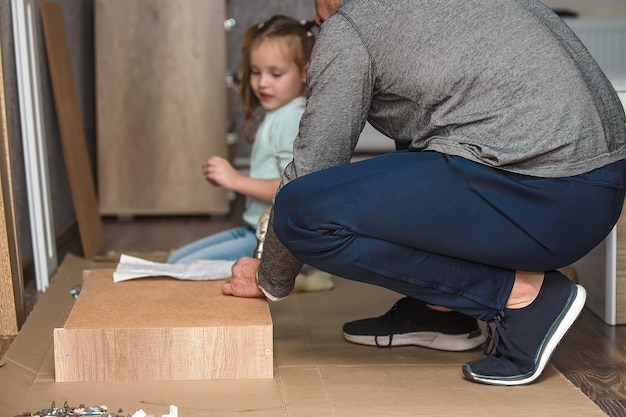 Ein Mann baut zu Hause mit seinen eigenen Händen Möbel zusammen und seine kleine Tochter hilft ihm dabei