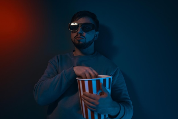 Ein Mann befindet sich in einem dunklen Raum mit Neonbeleuchtung und schaut sich einen Film mit einer D-Brille und hochwertigem Popcorn an
