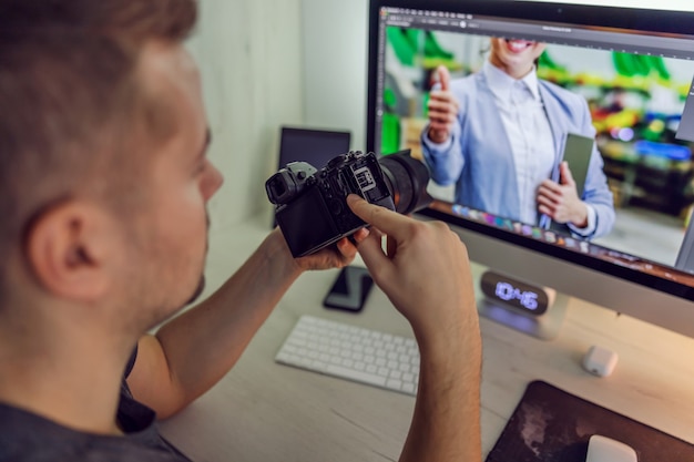 Ein Mann bei der Arbeit hält eine Kamera in den Händen, während er einen digitalen Computerbildschirm mit einem Foto betrachtet, das er aufgenommen hat