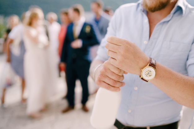 Ein Mann bei einer Hochzeitszeremonie öffnet eine Flasche Champagner hinter ihm Gäste und Jungvermählten Nahaufnahme