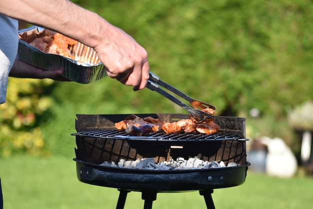 Ein Mann benutzt Pinzette, um Hühnerbeine auf einem Grill im Hintergarten vorzubereiten