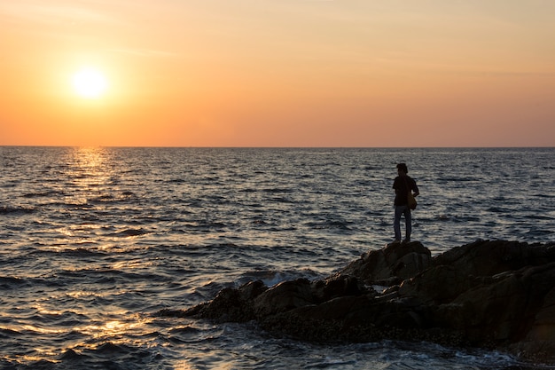 ein Mann beobachtet einen wunderschönen Sonnenuntergang über dem Meer auf einem Felsen