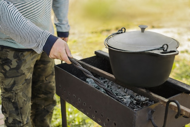 Foto ein mann bereitet essen in einem alten gusseisernen kessel auf dem grill zu. kochen in der natur