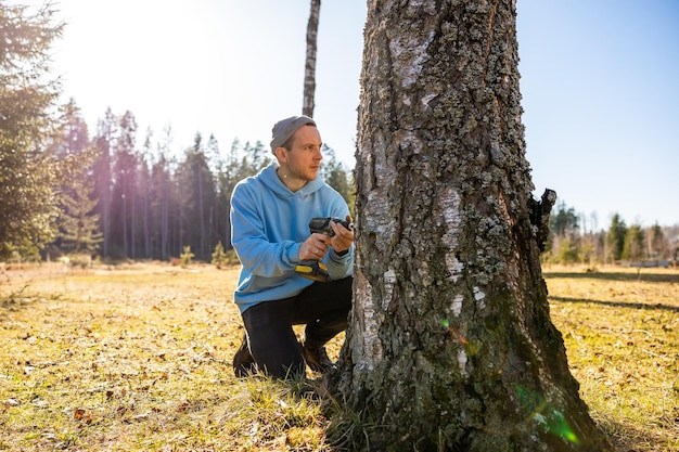 Ein Mann bohrt in einen Birkenbaum, um frischen Saft an einem hellen Frühlingstag zu sammeln