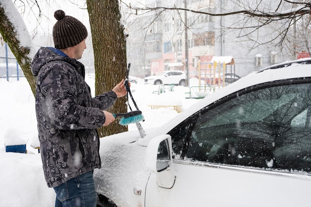 Ein Mann bürstet nach einem Schneefall Schnee von einem Auto Verkehrssicherheit schwierige Wetterbedingungen im Winter