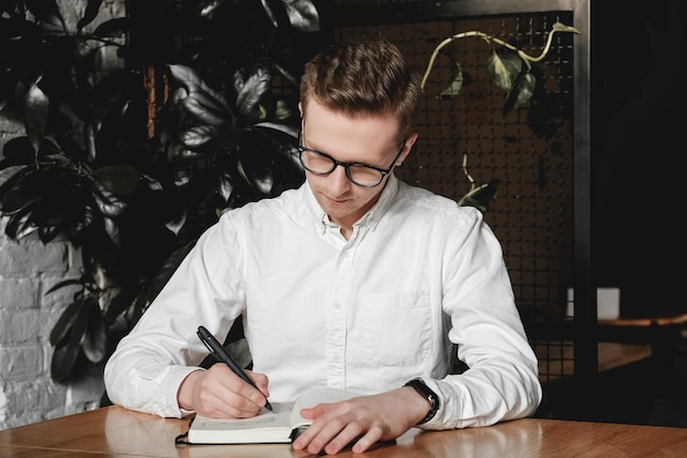 Ein Mann, der am Tisch sitzt und einen Stift hält, macht sich auf dunklem Hintergrund im Büro Notizen zu seiner Agenda