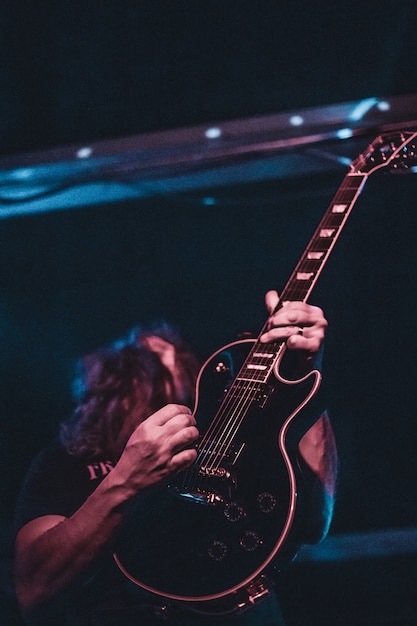 Ein Mann, der auf der Bühne Gitarre spielt. Dunkler Hintergrund, Scheinwerfer.