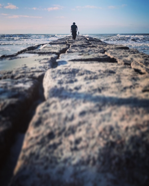 Foto ein mann, der auf einem felsen durch das meer gegen den himmel geht