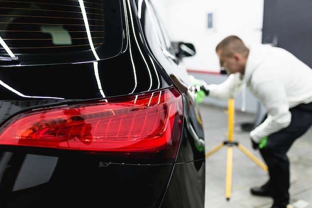 Ein Mann, der Auto mit Mikrofasertuch, Autodetaillierungs- (oder Reinigungskonzept) säubert. Selektiver Fokus.