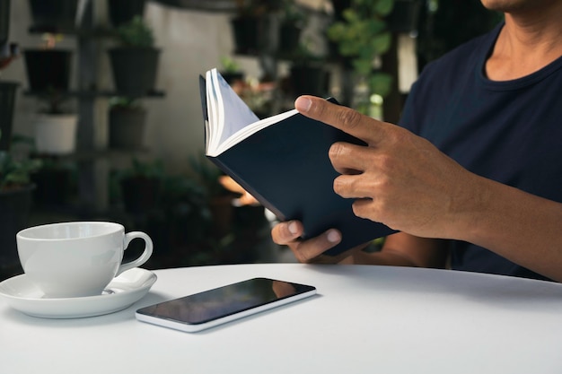 Ein Mann, der ein Buch mit Kaffeetasse liest. Mann sitzt im Stuhl zu Hause, liest Buch und entspannt.