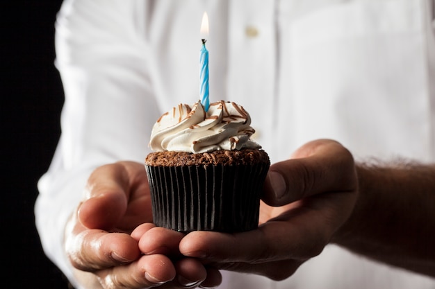 Ein Mann, der einen Cupcake mit einer Kerze in einer Geste des Gebens hält.