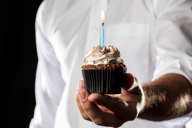 Ein Mann, der einen Cupcake mit einer Kerze in einer Geste des Gebens hält.