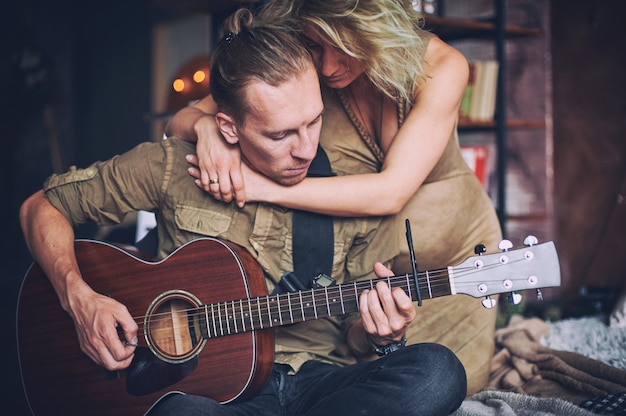 Ein Mann, der Gitarre spielt, und seine schwangere Frau sitzen auf einem Bett in einem Dachbodenzimmer