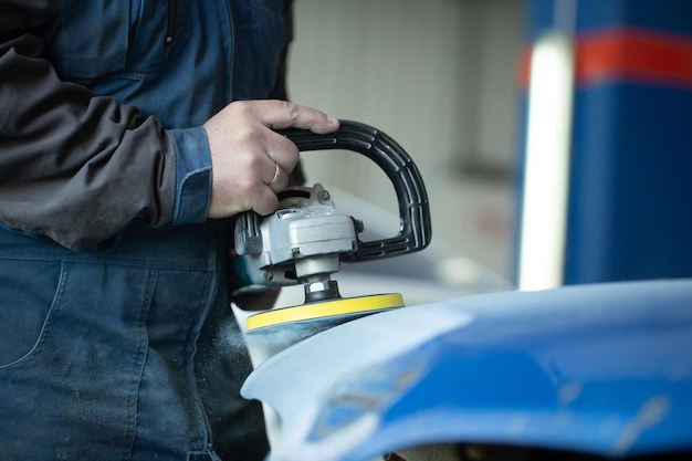 Ein Mann, der in einem Autoservice mit einer Schleifmaschine schleift und den Lack für das Auto vorbereitet