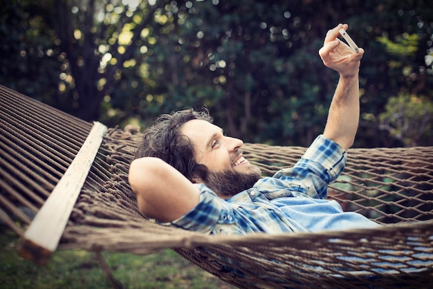 Ein Mann, der in einer Gartenhängematte liegt und Selfies mit seinem Telefon macht