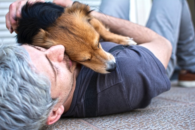 Ein Mann, der liegt und seinen Hund umarmt, der ihn auf seiner Brust liegen hat.