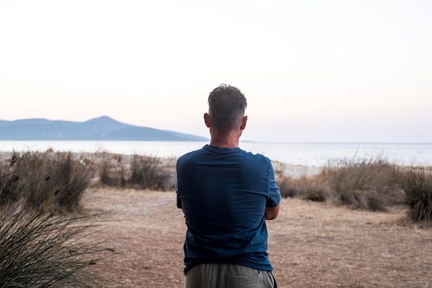 Ein Mann, der von hinten in der Landschaftsbetrachtung betrachtet wird. Ein Tourist sieht aus wie ein malerischer Ort mit Meer und Insel. Reisen, Menschen, Lifestyle-Konzept, Freiheit, blaue Stimmung, Himmel und Meer, nicht wiederzuerkennender Mann