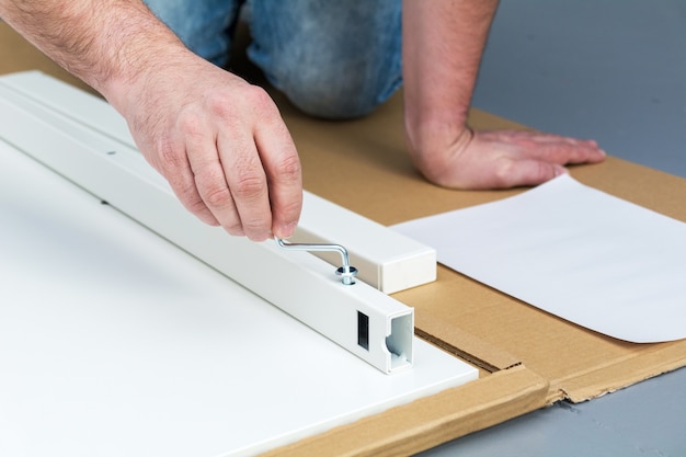 Ein Mann, ein Handwerker in einem blauen Hemd, sammelt einen Tisch in Nahaufnahme