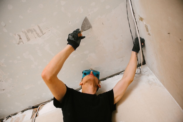 Ein Mann entfernt alte Farbe mit einem Spatel von der Decke