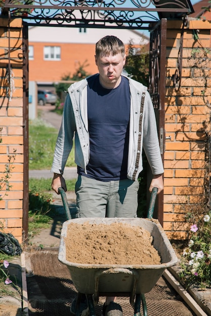 Ein Mann entlädt Sand in eine Zementmischung zum Gießen eines Gartenweges, Bauarbeiten auf einem Gartengrundstück