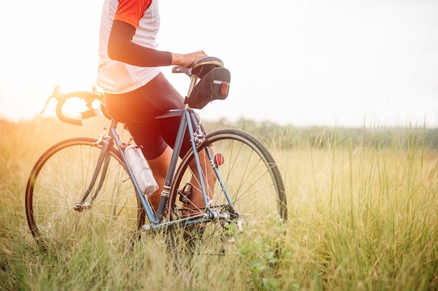 Ein Mann fährt mit dem Fahrrad auf der Straße. Mann reitet Vintage-Sportfahrrad für Abendübungen. Ein Mann fährt Fahrrad, um die frische Luft inmitten von Natur, Wiese, Wald, mit durchscheinender Abendsonne zu atmen