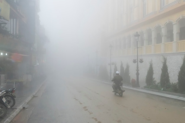 Ein Mann fährt mit seinem Motorrad durch dichten Nebel in der Stadt. Sapa, Vietnam,