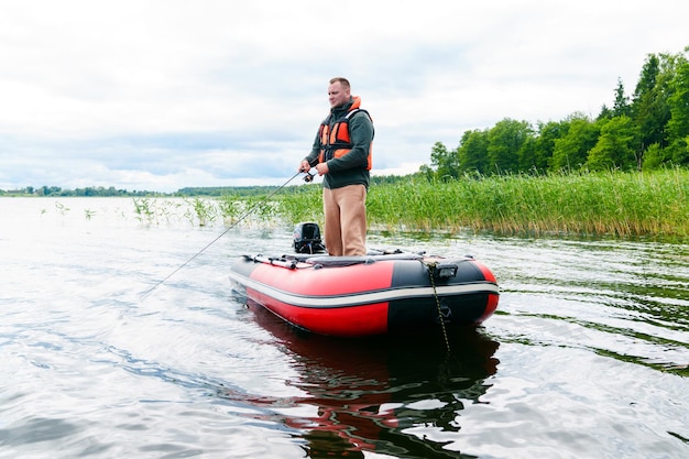 Ein Mann fischt im Stehen von einem Schlauchboot aus. Der See hat klares Wasser. Hobbys und Erholung