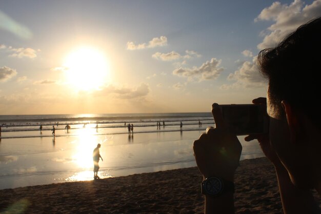 Foto ein mann fotografiert menschen, die sich beim sonnenuntergang am strand erfreuen