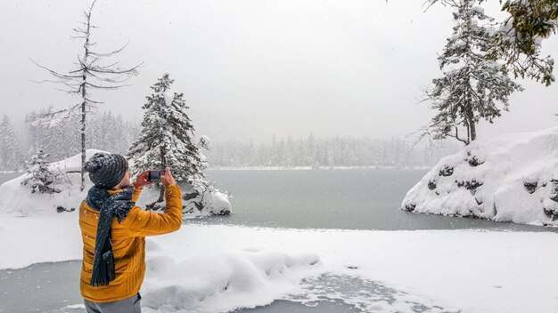 Foto ein mann fotografiert, während er im winter am schnee bedeckten land am see steht