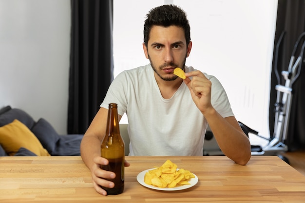 Ein Mann führt einen falschen Lebensstil, er isst Pommes und trinkt Bier.