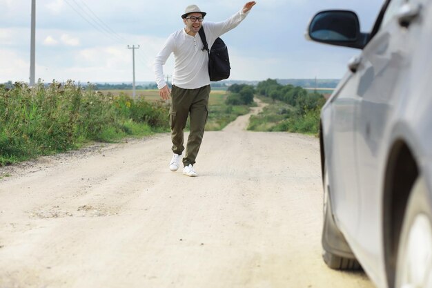 Ein Mann geht auf einer Landstraße per Anhalter durchs Land Ein Mann hält ein vorbeifahrendes Auto auf der Straße an