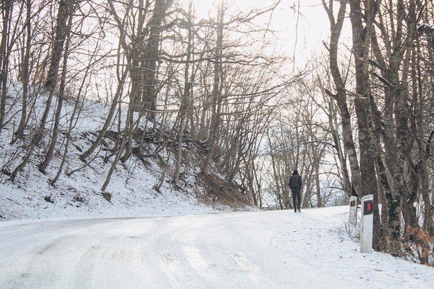 Ein Mann geht im Winter im Wald die Straße entlang