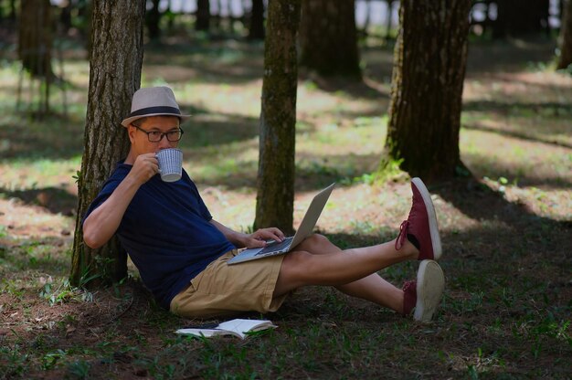 Ein Mann genießt seine Freizeit und arbeitet an seinem Laptop unter einem Baum im Kiefernwald