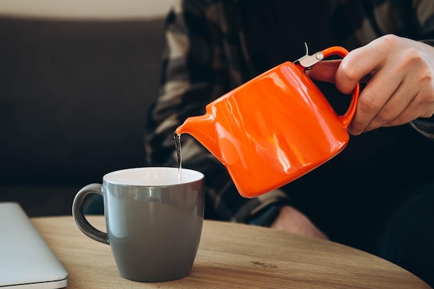 Ein Mann gießt Tee aus einer leuchtend orangefarbenen Teekanne in eine Tasse