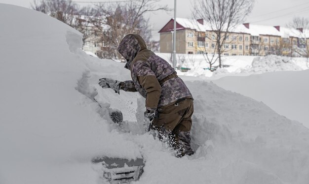 Ein Mann gräbt sein Auto nach einem schweren Schneesturm mit Schnee bedeckt aus dem Schnee