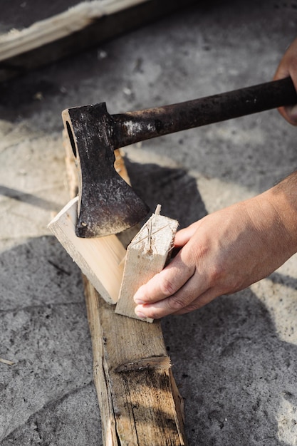 Ein Mann hackt Holz mit einer Axt, um ein Feuer anzuzünden. Hinterhofarbeit