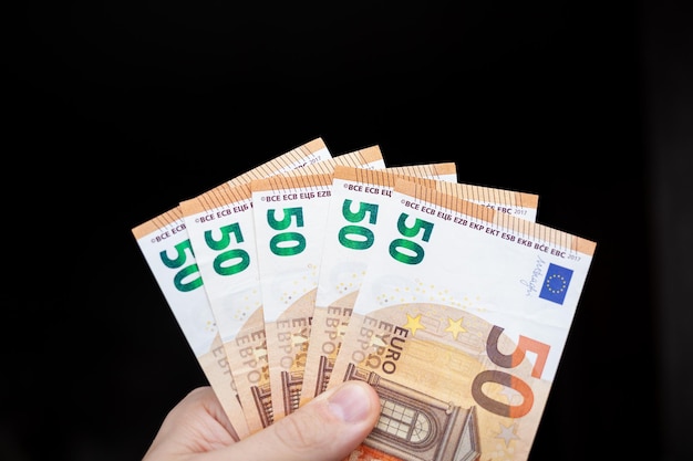 Ein Mann hält 100-Euro-Banknoten auf dunklem Hintergrund in der Hand