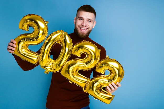 Ein Mann hält die Zahlen 2022 aus goldenen Ballons. Das kommende neue Jahr