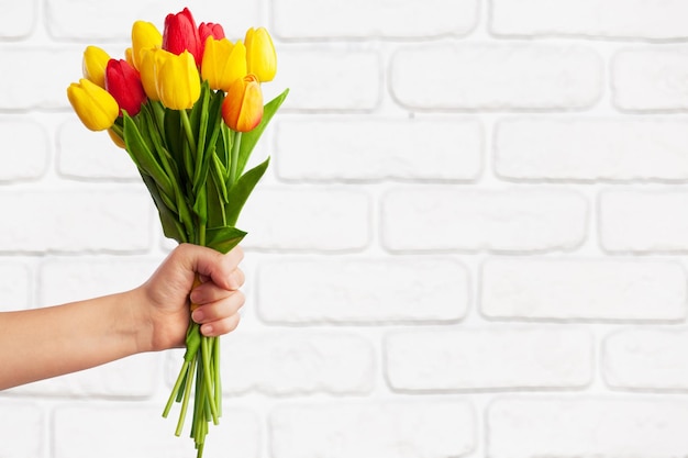 Ein Mann hält ein Bouquet an schönen Frühlings-Tulpen in der Nähe einer Backsteinmauer