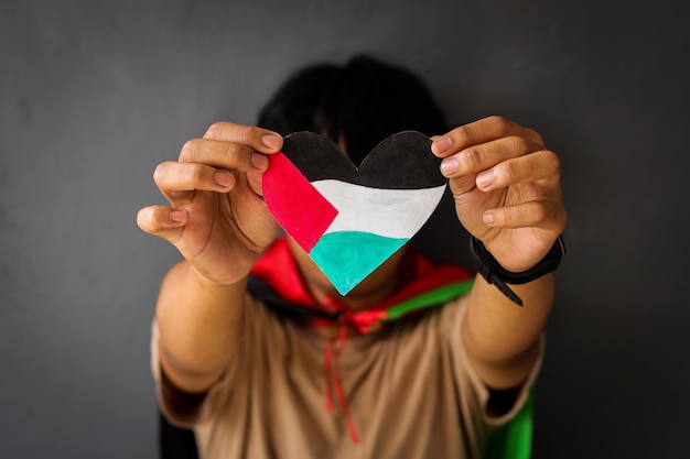 Foto ein mann hält ein herzförmiges papier, das die palästinensische flagge symbolisiert, und zeigt es der kamera