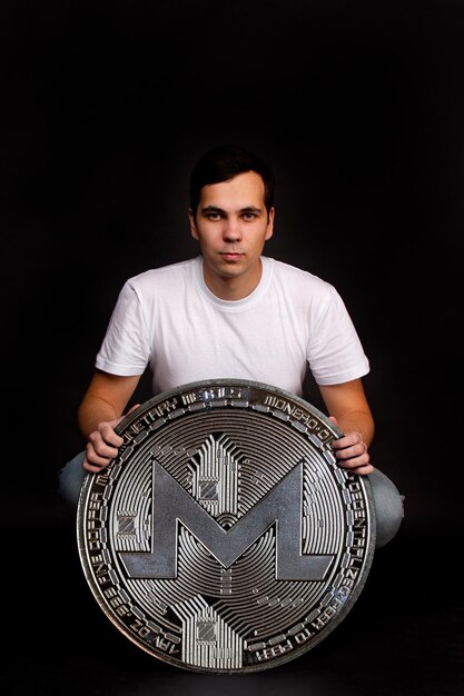 Ein Mann hält eine Monero-Münze in seinen Händen als Symbol für Technologie Bild auf schwarzem Hintergrund