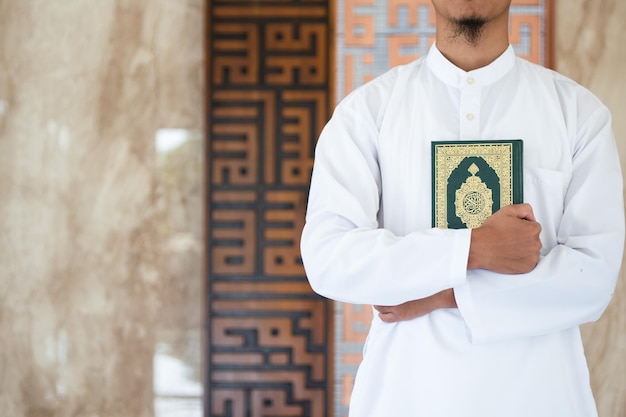 Foto ein mann hält einen grünen koran mit der aufschrift „koran“ vor eine wand.