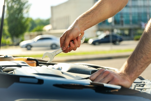 Ein Mann hält einen Schraubenschlüssel über einen Automotor. Autoinspektion