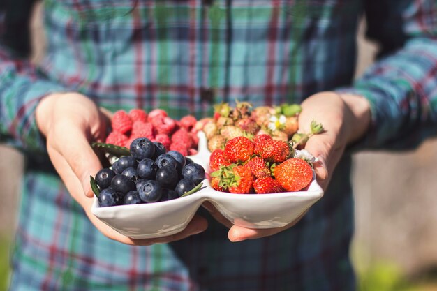 Ein Mann hält einen Teller mit verschiedenen Beeren, der richtigen Ernährung und Vitaminen in den Händen