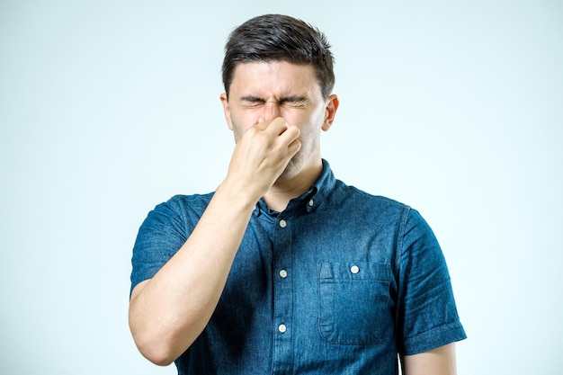 Ein Mann hält seine Nase vor einem schlechten Geruch vor einem grauen Hintergrund
