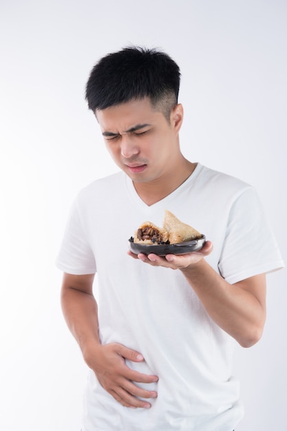 Ein Mann hat Bauchschmerzen, nachdem er köstliche Zongzi (Reisknödel) auf Drachenbootfest gegessen hat, asiatisches traditionelles Essen, weißer Hintergrund