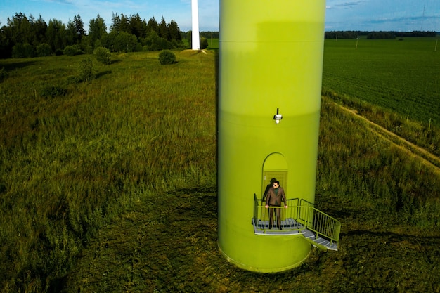 Ein Mann im Anzug mit grünem Golfhemd steht neben einer Windmühle vor dem Hintergrund des Feldes und des blauen Himmels. Geschäftsmann in der Nähe der Windmühlen. Modernes Konzept der Zukunft.