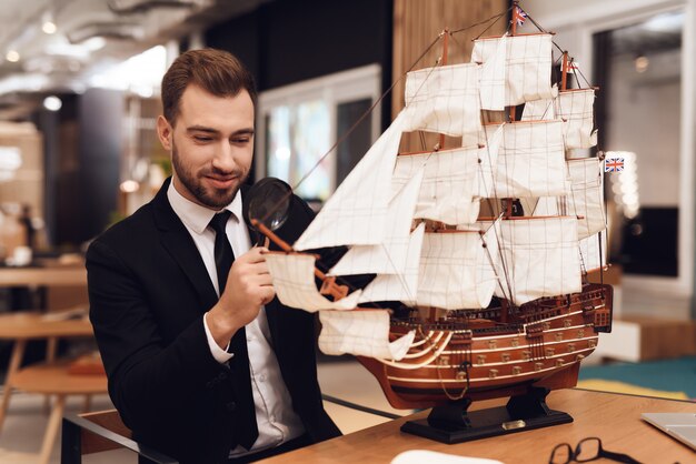 Ein Mann im Anzug sitzt mit einem Segelboot an einem Tisch.