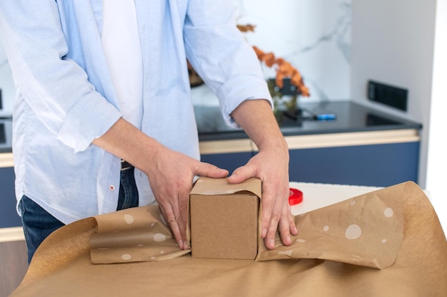 Ein Mann im Hemd, der in der Küche steht, packt eine Geschenkbox in Kraftpapier