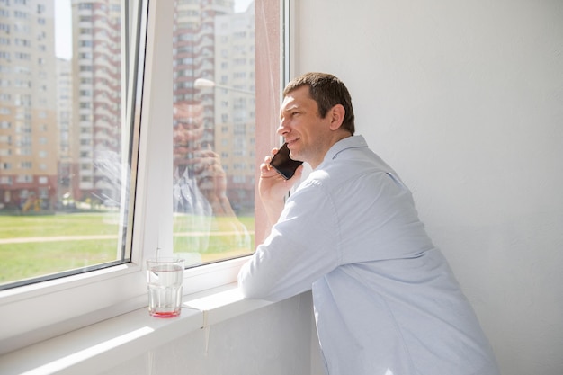 Ein Mann im Hemd steht auf dem Balkon am Fenster und telefoniert